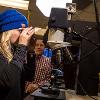 A woman looks through a microscope while a man stands to her side in the forensics lab