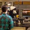 The back of a man is seen looking into a microscope next to a computer screen showing images