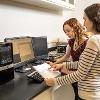 Two women stand at a desk and analyze a graph they have printed from the computer