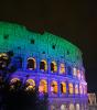 A photo of a colosseum at night lit up by a mix of purple and green.