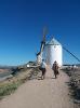 A photo of two people walking across a sparse landscape towards a windmill.