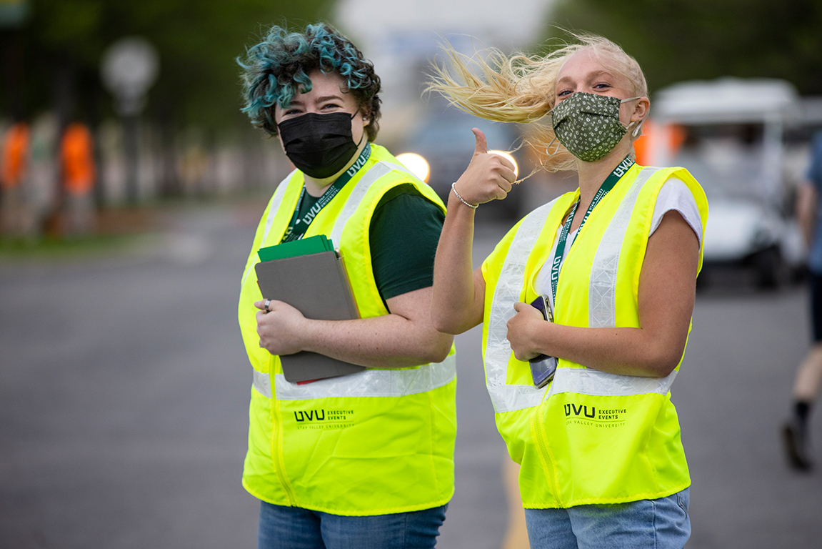 Two event ambassadors in yellow vests help direct parking at commencement. One gives the camera a thumbs up.