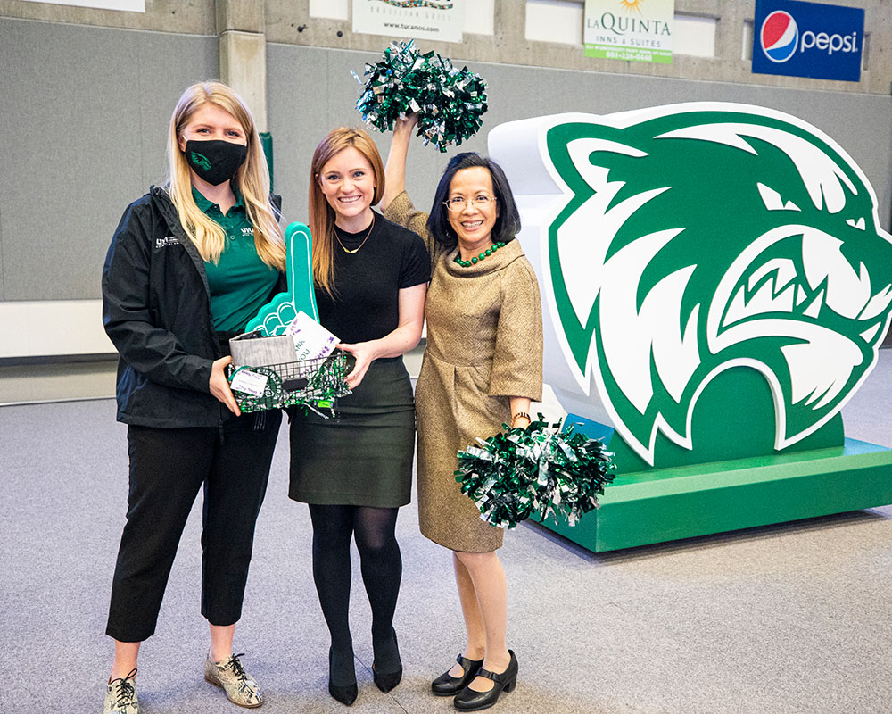 President Astrid Tuminez waves green pom-poms with two events coordinators at the doTerra Performance Center Ribbon Cutting.