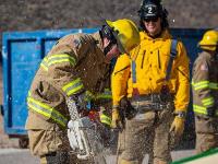 Firefighters cutting through plywood with a chainsaw.