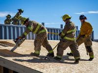 Firefighters cutting through plywood with a chainsaw.