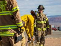 Firefighters cutting through plywood with a chainsaw.