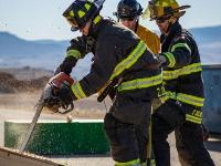 Firefighters cutting through plywood with a chainsaw.