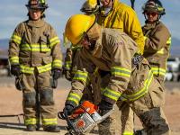 Firefighters cutting through plywood with a chainsaw.