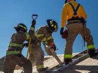 Firefighters cutting through plywood with a chainsaw.