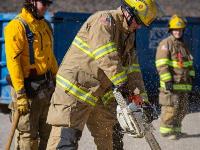 Firefighters cutting through plywood with a chainsaw.