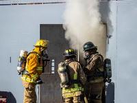 Three firefighters standing outside a door with smoke coming out of it