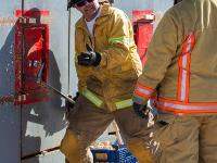 Firefighter prying open metal door while another firefighter watches