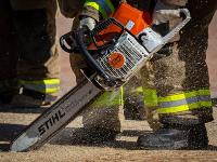 Firefighters cutting through plywood with a chainsaw.