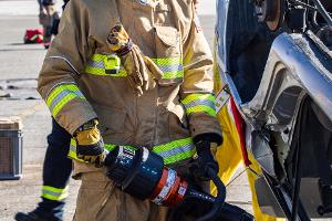 Firefighters gathered around a burnt car using a Hydraulic rescue tool