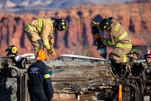 Group of firefighters next to a overturned car looking a mountain