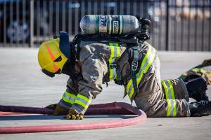 Firefighter kneeling on the ground holding a firehose