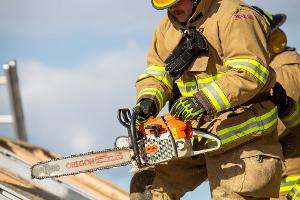 Firefighters cutting through plywood with a chainsaw