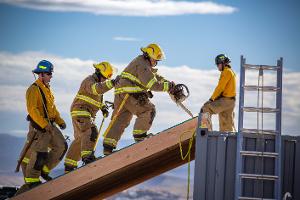 Firefighters cutting through plywood with a chainsaw