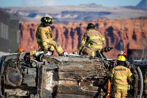 Group of firefighters next to a overturned car looking a mountain