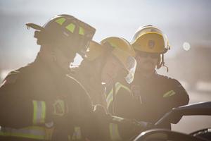 Firefighters gathered around a burnt car using a Hydraulic rescue tool