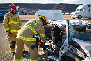 Firefighters gathered around a burnt car using a Hydraulic rescue tool