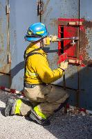 Firefighters prying open a red metal box with a crowbar