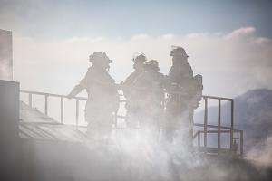 Firefighters standing on top of smoking building