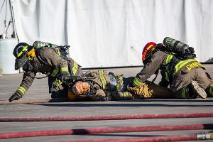 Firefighters kneeling on the ground holding a firehose