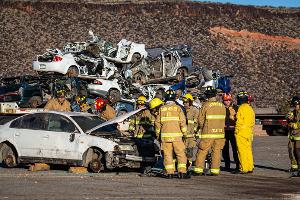 Firefighters gathered around a burnt car using a Hydraulic rescue tool