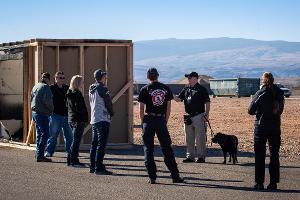 People gathered together listening to instruction from a man with a dog on a leash