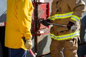 Firefighters prying open a red metal box with a crowbar