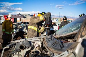 Firefighters gathered around a burnt car using a Hydraulic rescue tool