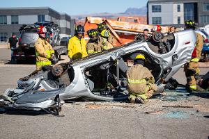 Firefighters gathered around a burnt car using a Hydraulic rescue tool