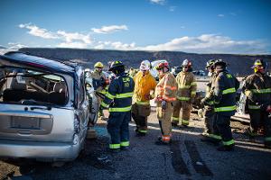 Firefighters gathered around a burnt car using a Hydraulic rescue tool