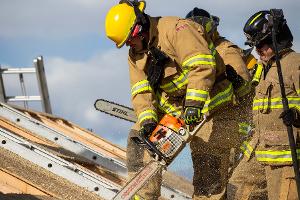 Firefighters cutting through plywood with a chainsaw