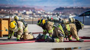 Three firefighters on kneeling on the ground holding onto a hose