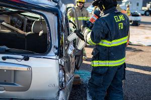 Firefighters gathered around a burnt car using a Hydraulic rescue tool