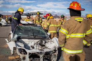 Firefighters gathered around a burnt car using a Hydraulic rescue tool