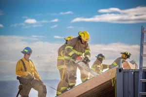 Firefighters cutting through plywood with a chainsaw