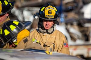 Firefighters gathered around a burnt car using a Hydraulic rescue tool