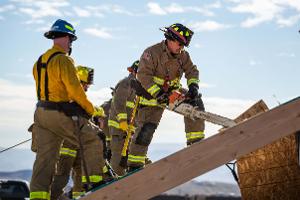 Firefighters cutting through plywood with a chainsaw