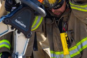 Firefighters gathered around a burnt car using a Hydraulic rescue tool