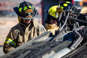 Firefighters gathered around a burnt car using a Hydraulic rescue tool