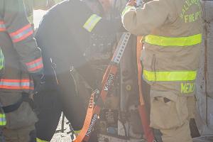 Firefighters gathered around a burnt car using a Hydraulic rescue tool