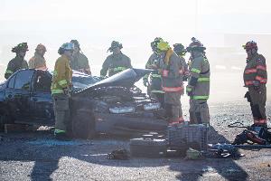 Firefighters gathered around a burnt car using a Hydraulic rescue tool