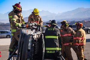 Firefighters gathered around a car listening to instruction.