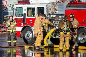 Firefighters holding a firehose next to a firetruck