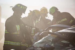 Firefighters gathered around a burnt car using a Hydraulic rescue tool