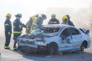 Firefighters gathered around a burnt car using a Hydraulic rescue tool