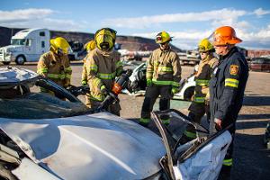 Firefighters gathered around a burnt car using a Hydraulic rescue tool